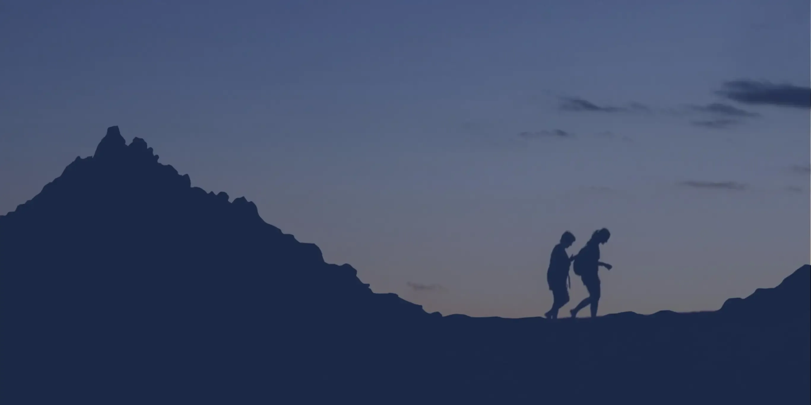 Two individuals walking on a mountain trail during dusk